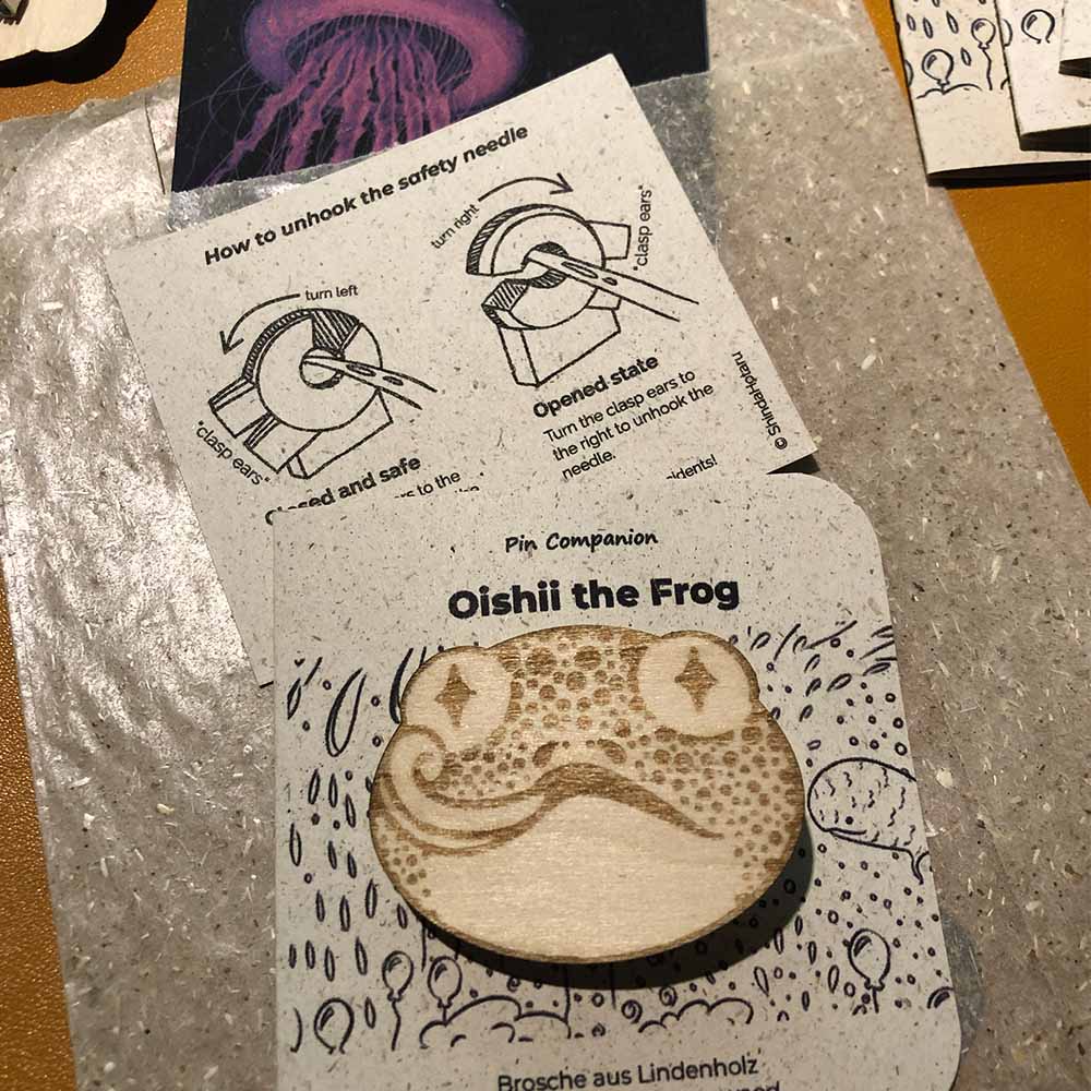Holzanstecker eines Froschkopfes mit dazugehöriger Hinweiskarte zum Öffnen des Verschlusses.