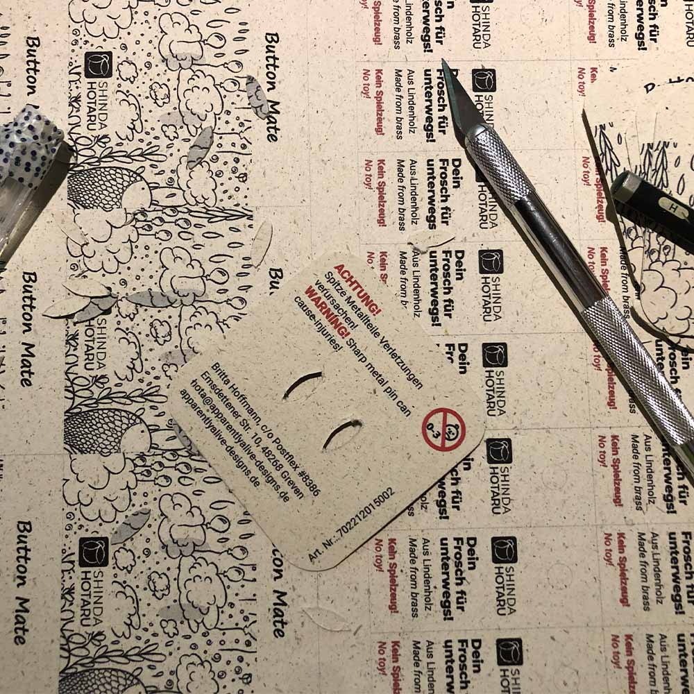 Auf einem bedruckten Papier mit Etikett liegt eine Rückkarte (Backing Card) und ein Bastelmesser.